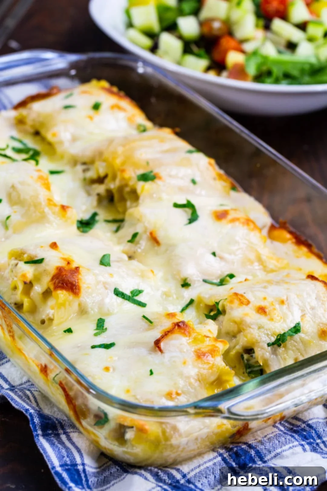 Alfredo Chicken Lasagna Pinwheels 3 A baking dish filled with golden-brown Chicken Alfredo Lasagna Roll-Ups, alongside a fresh green salad, highlighting a complete meal.