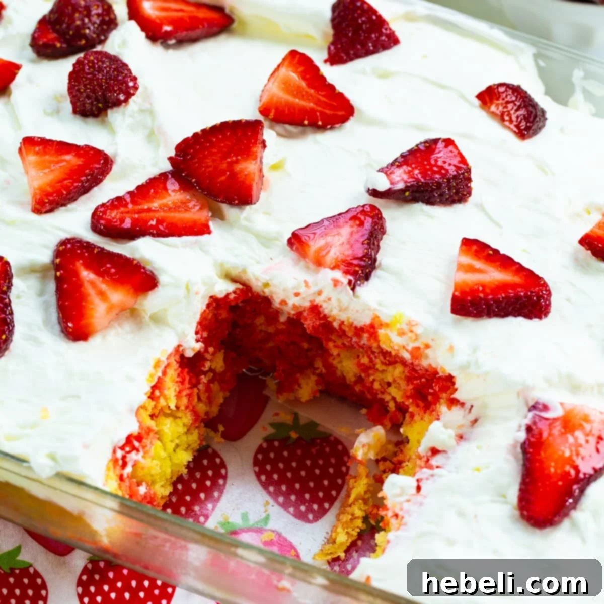 A baked cake in a 9x13 inch baking pan with one slice already removed, showing the internal layers of lemon cake and strawberry gelatin filling.