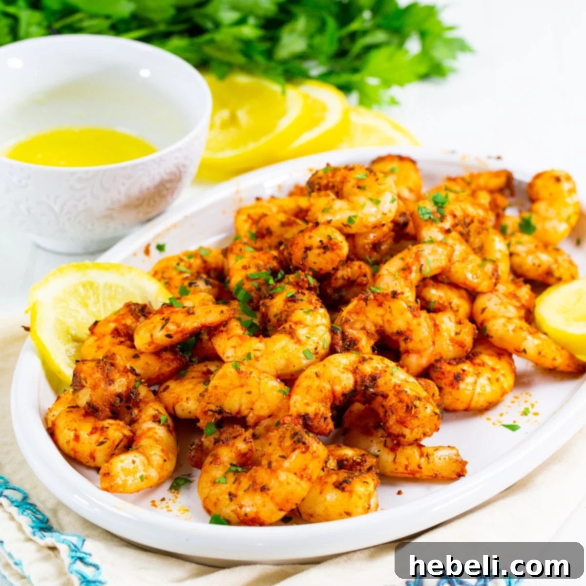 Platter of perfectly cooked Air Fryer Cajun Shrimp, garnished with fresh parsley and lemon slices.