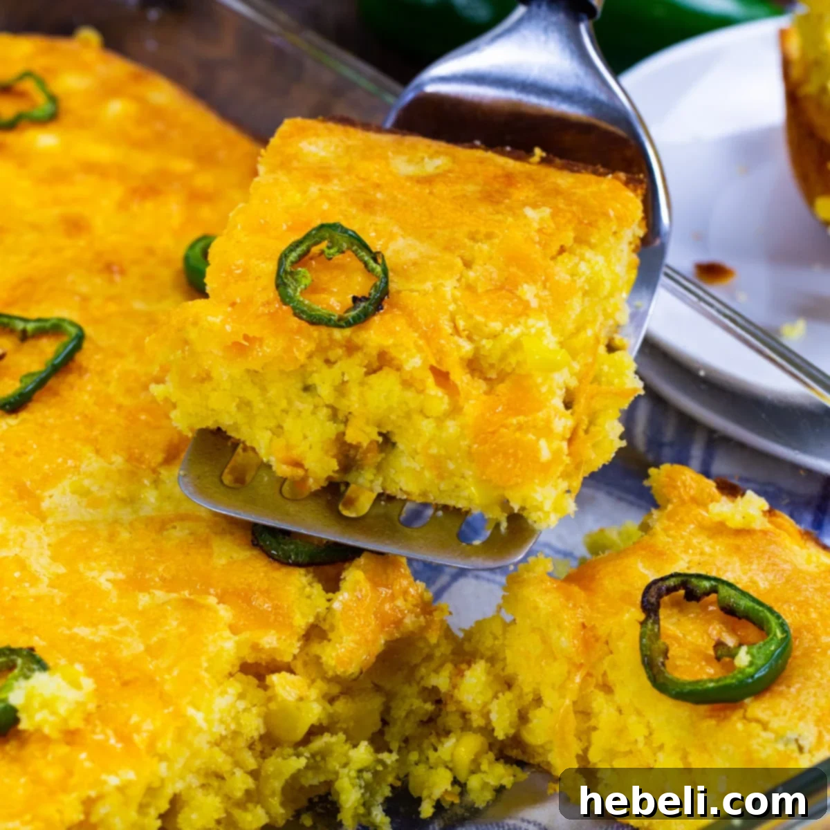 Spatula lifting a golden piece of Texas-Style Jiffy Cornbread, revealing its moist texture and delicious additions of corn, jalapenos, and cheddar cheese.