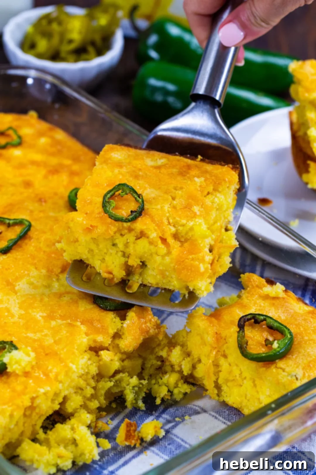 A spatula lifting a generous piece of Texas-Style Jiffy Cornbread from the baking dish, showcasing its perfect cut, crispy edges, and delicious melted cheese topping.