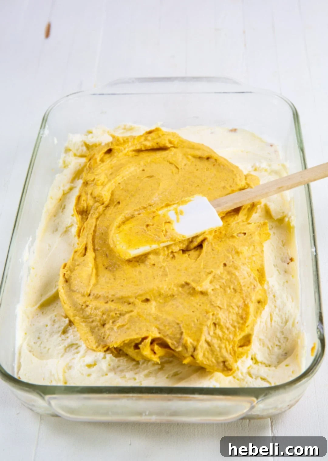 Decadent Pumpkin Delight 4 Spreading the smooth orange pumpkin layer evenly over the pristine white cream cheese layer in a glass baking dish, highlighting the precision.