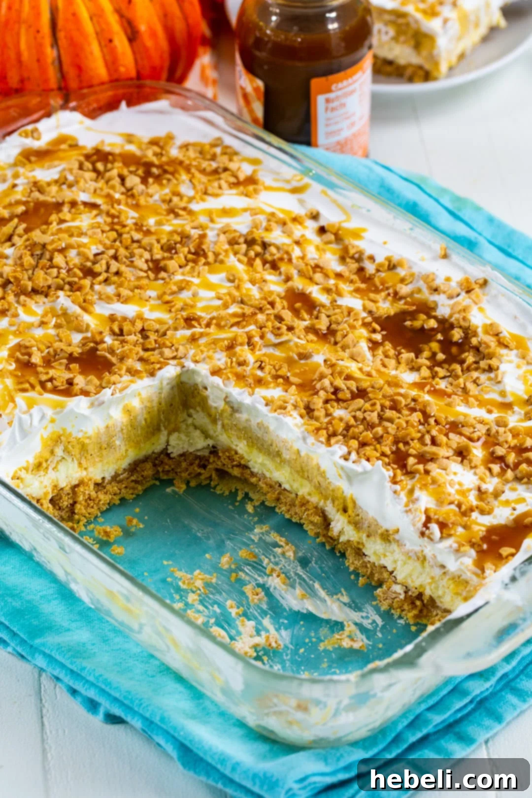 Decadent Pumpkin Delight 5 A slice of Pumpkin Lush removed from the pan, showing its distinct four layers, with the remaining dessert in the pan beautifully topped with caramel drizzle and scattered toffee bits.