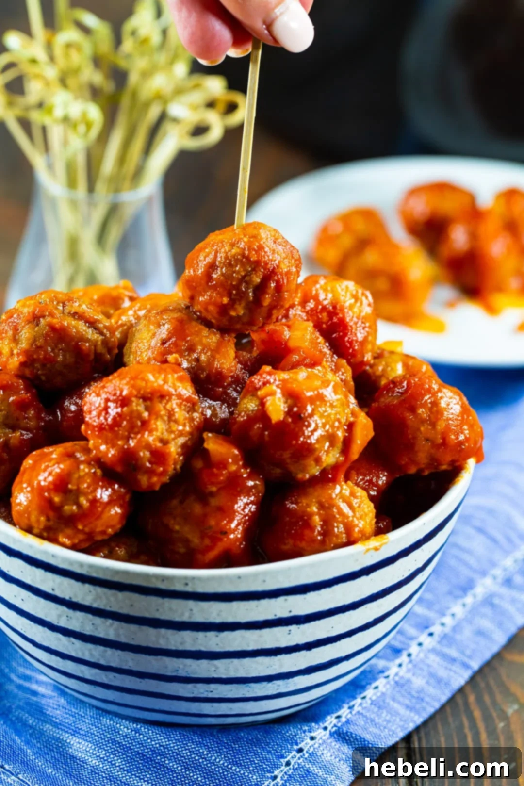 Tender Slow Cooker BBQ Meatballs 5 A hand picking up a glistening BBQ meatball with a toothpick, ready to eat.