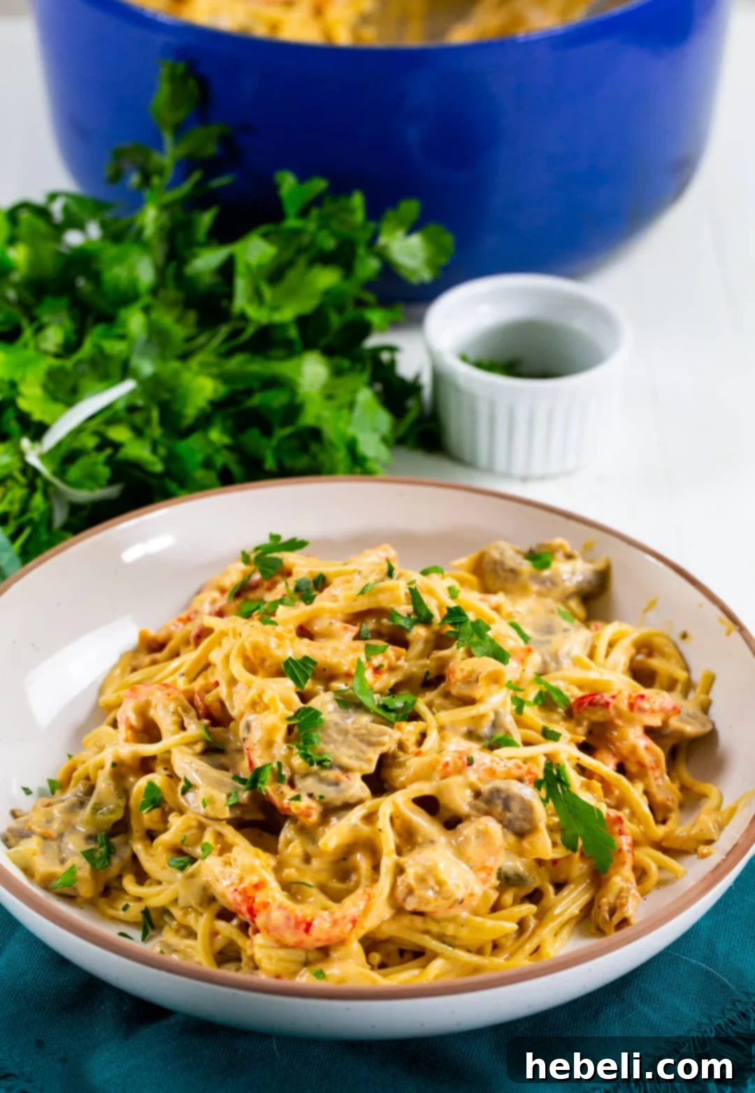 A close-up of a generous serving of Crawfish Tetrazzini in a white serving bowl, beautifully garnished with fresh green parsley.