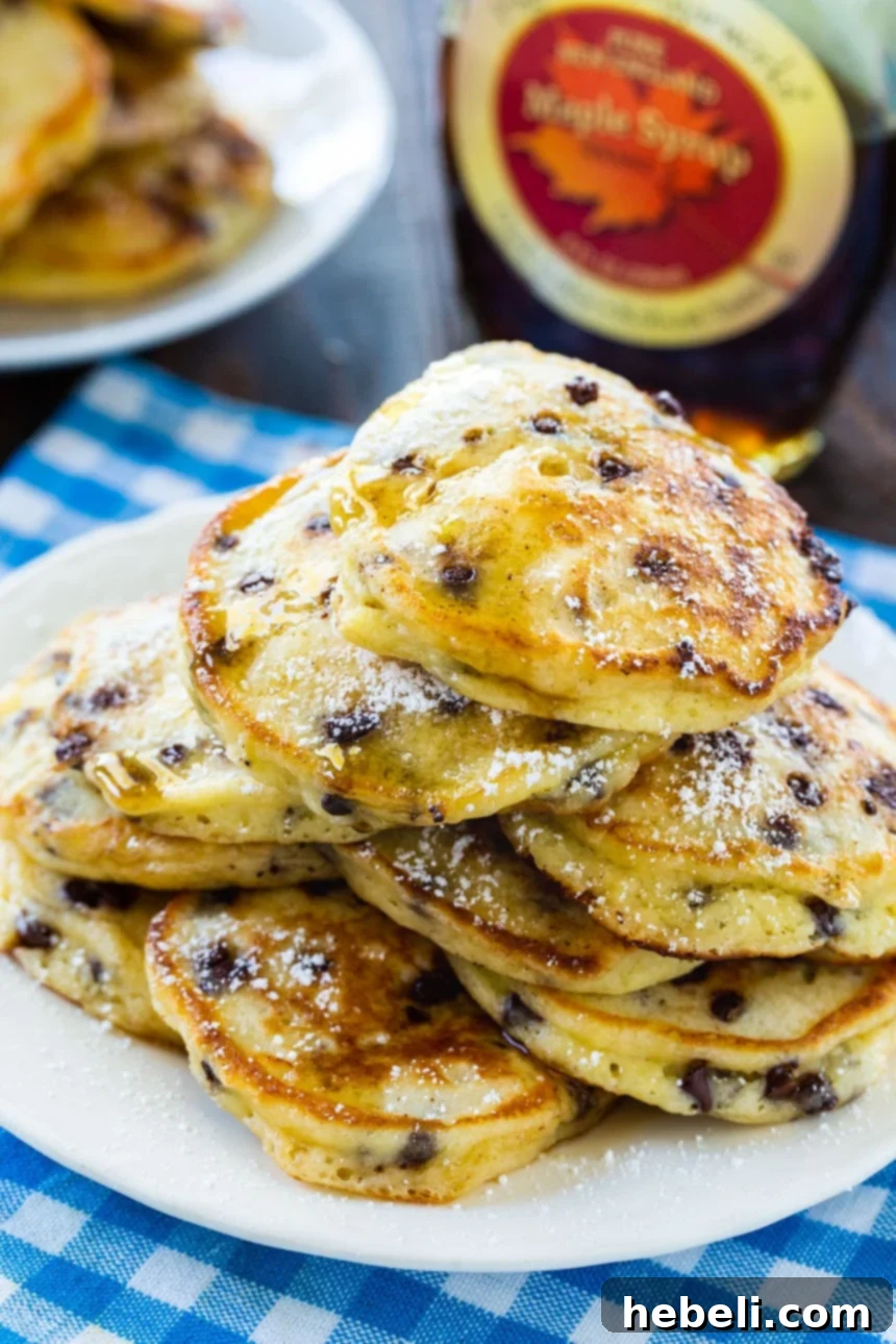 Tangy Mini Chocolate Chip Pancakes 3 Perfectly cooked Sour Cream Pancakes, glistening with maple syrup, on a white plate with a bottle of syrup in the background.