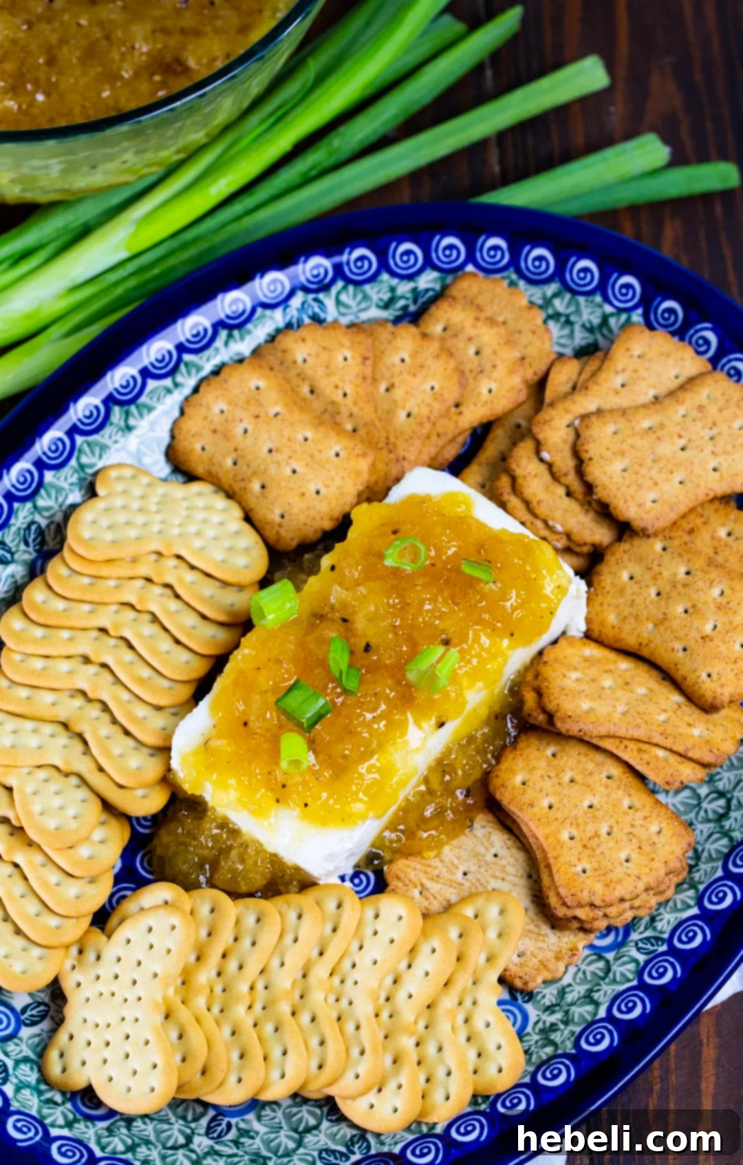 A festive holiday platter showcasing cream cheese lavishly topped with Jezebel Sauce, elegantly surrounded by an assortment of gourmet crackers.