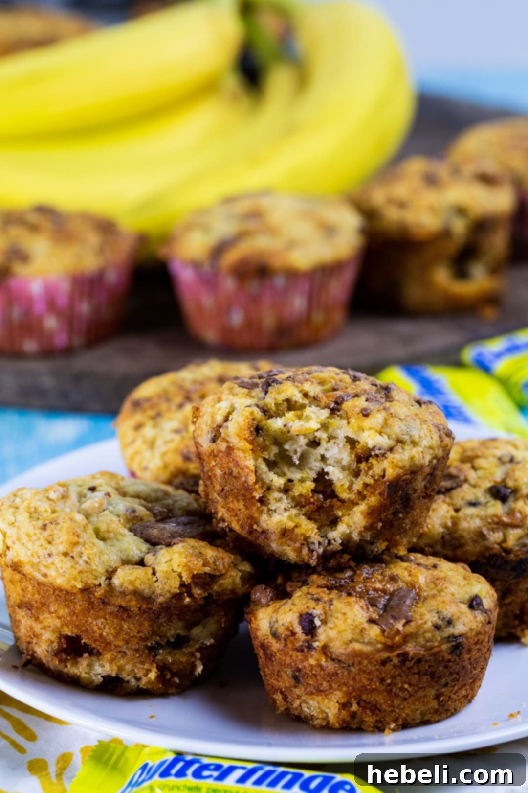 A single Butterfinger Banana Muffin with a bite taken out, revealing its moist interior, banana flecks, chocolate chips, and Butterfinger candy pieces.