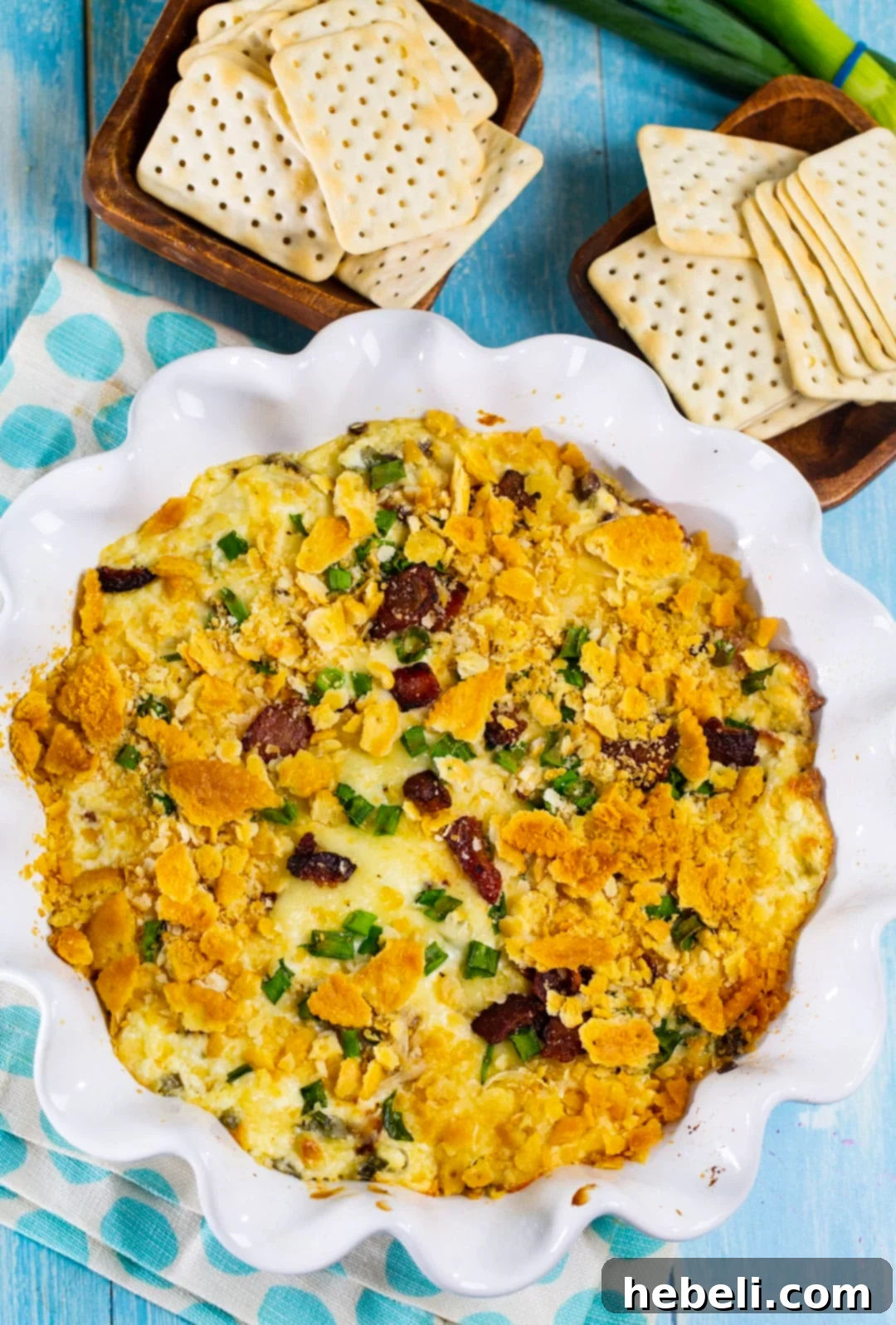 Bacon Swiss Dip surrounded by various crackers and serving utensils.
