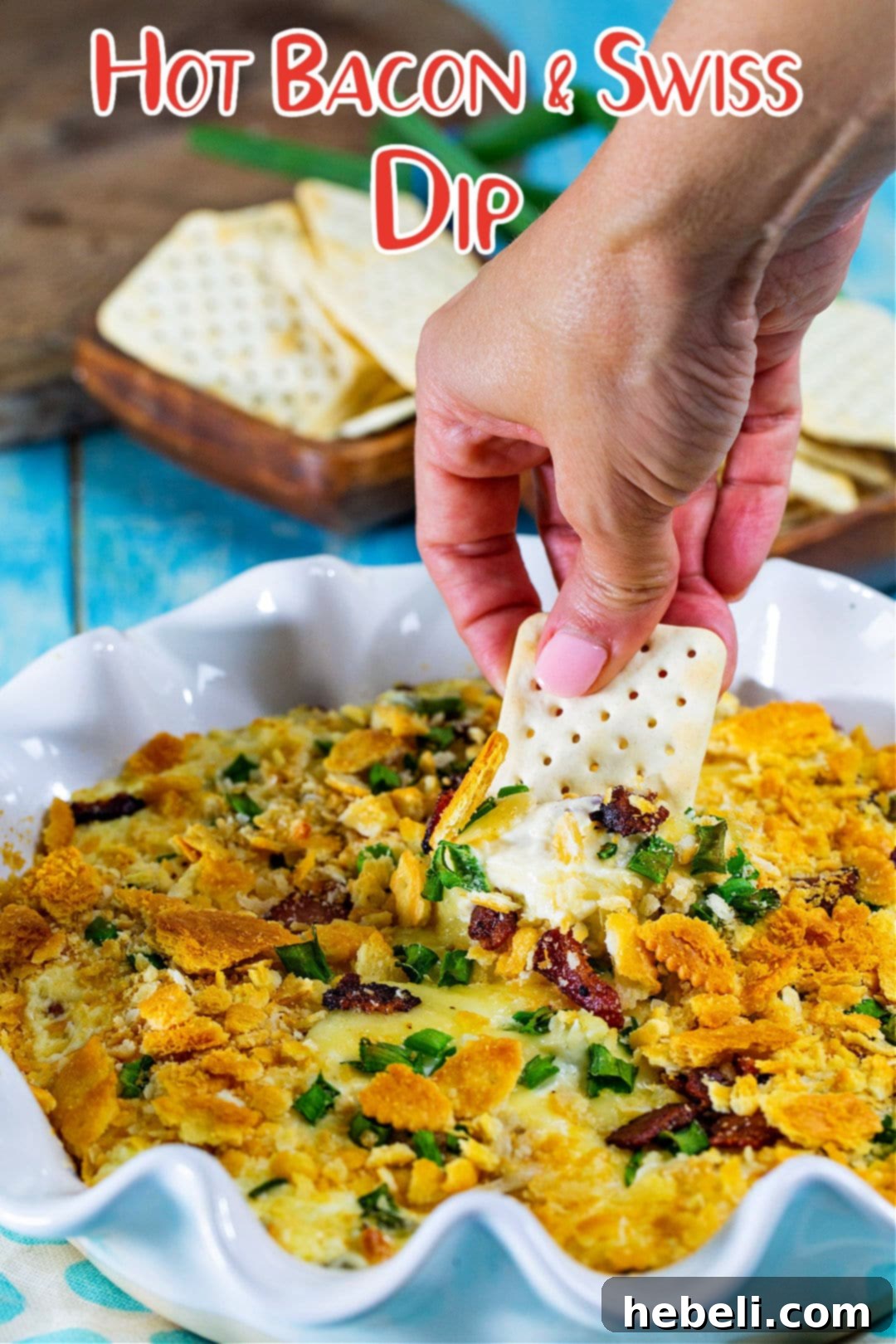 A hand dipping a cracker into the Hot Bacon and Swiss Dip, showing its inviting texture.