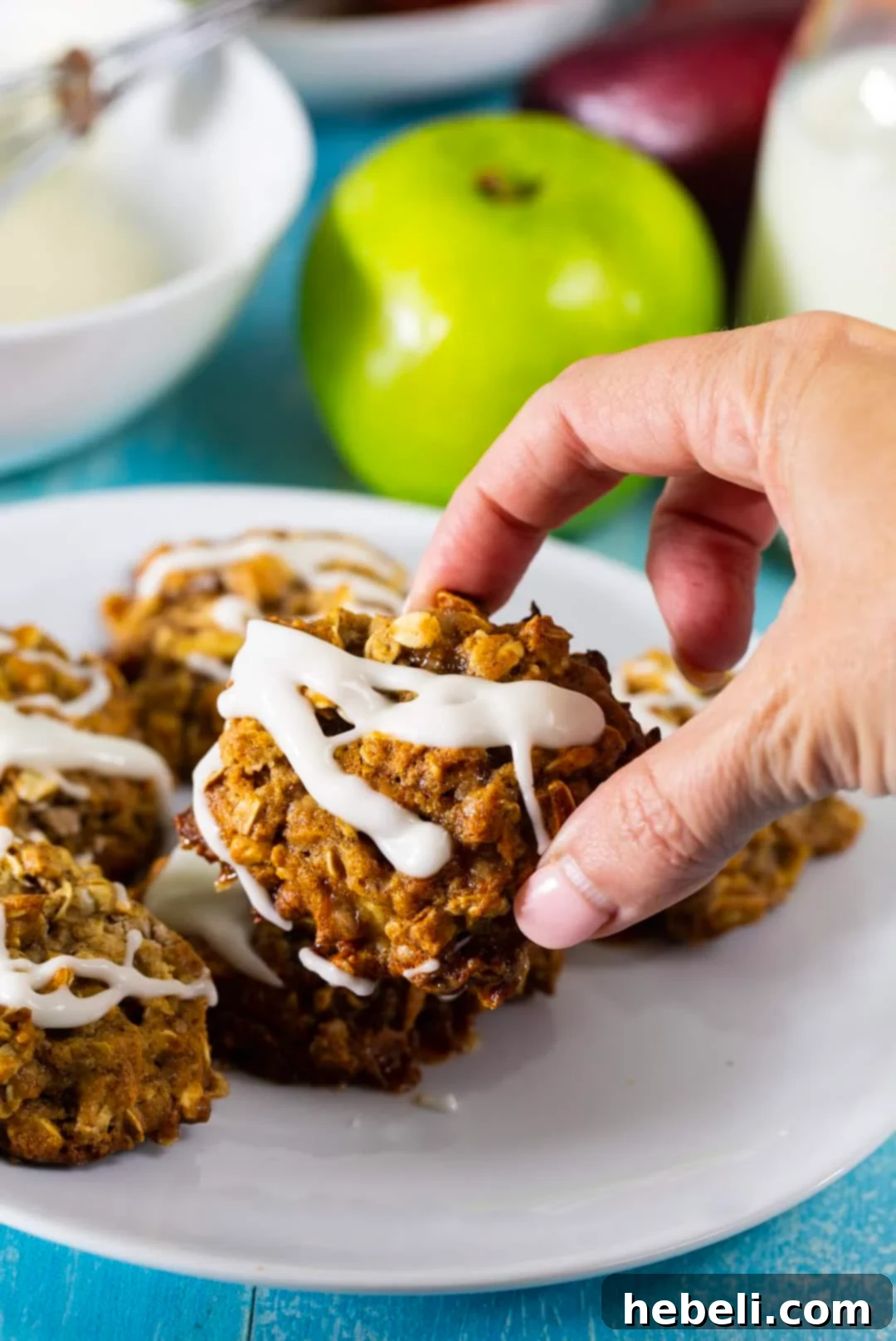 A hand reaching for a freshly baked Apple Toffee Oatmeal Cookie, showcasing its chewy texture.