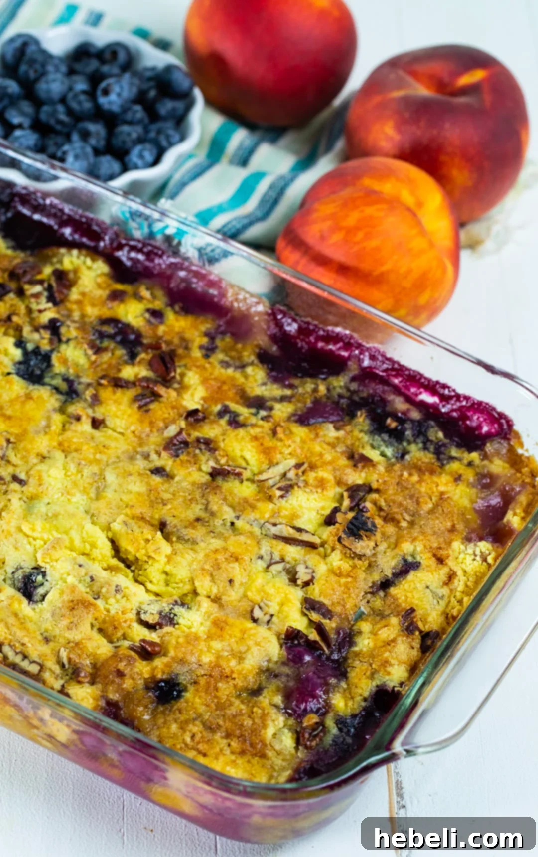 A vibrant display of fresh ingredients for Blueberry Peach Dump Cake, including a bowl full of plump blueberries, next to a 9x13-inch baking dish, illustrating the simple preparation process.