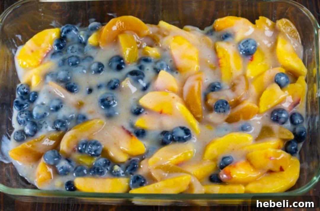 A close-up view of the prepared fruit filling with blueberries and sliced peaches perfectly arranged in a baking dish, ready for the next layer of cake mix.