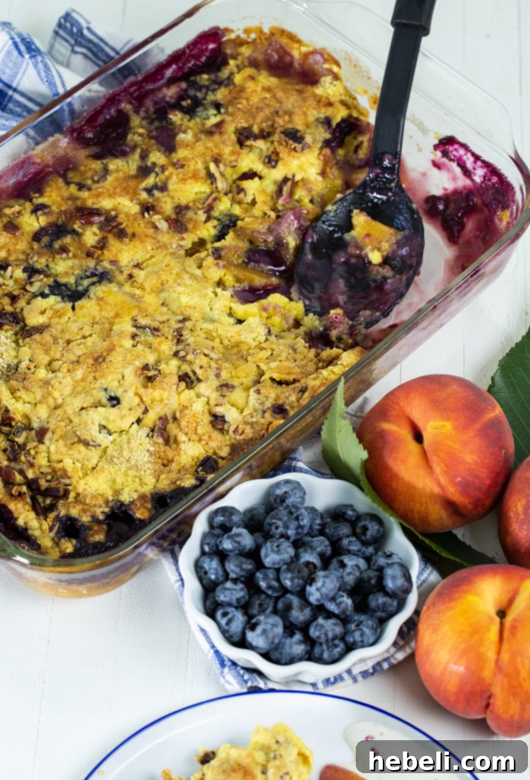 A serving spoon lifting a generous portion of warm, gooey Blueberry Peach Dump Cake from the baking dish, showcasing the luscious fruit filling and crunchy topping.