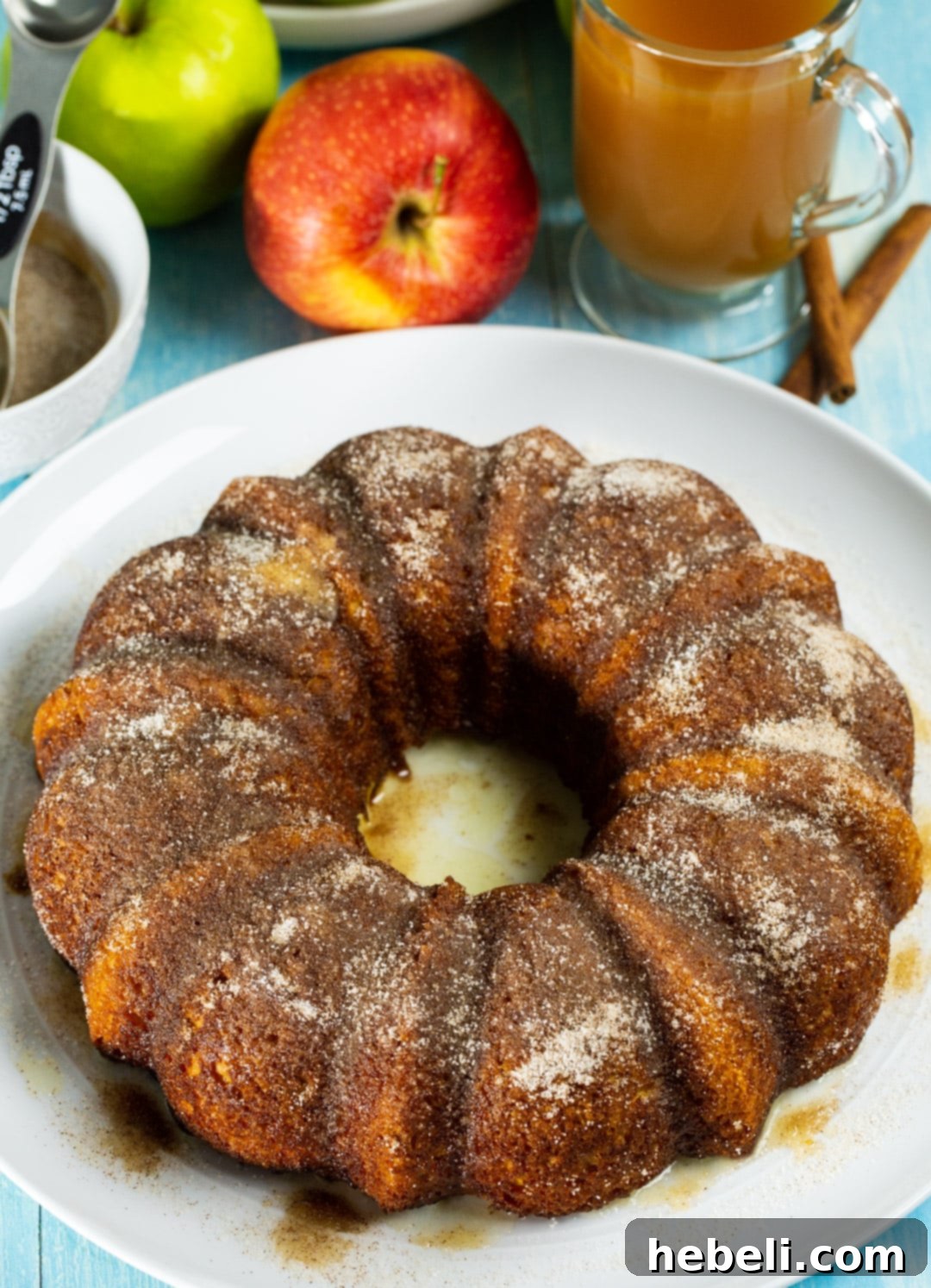 A beautifully baked Apple Cider Bundt Cake, glistening with its cinnamon sugar coating, presented on a rustic cake stand.