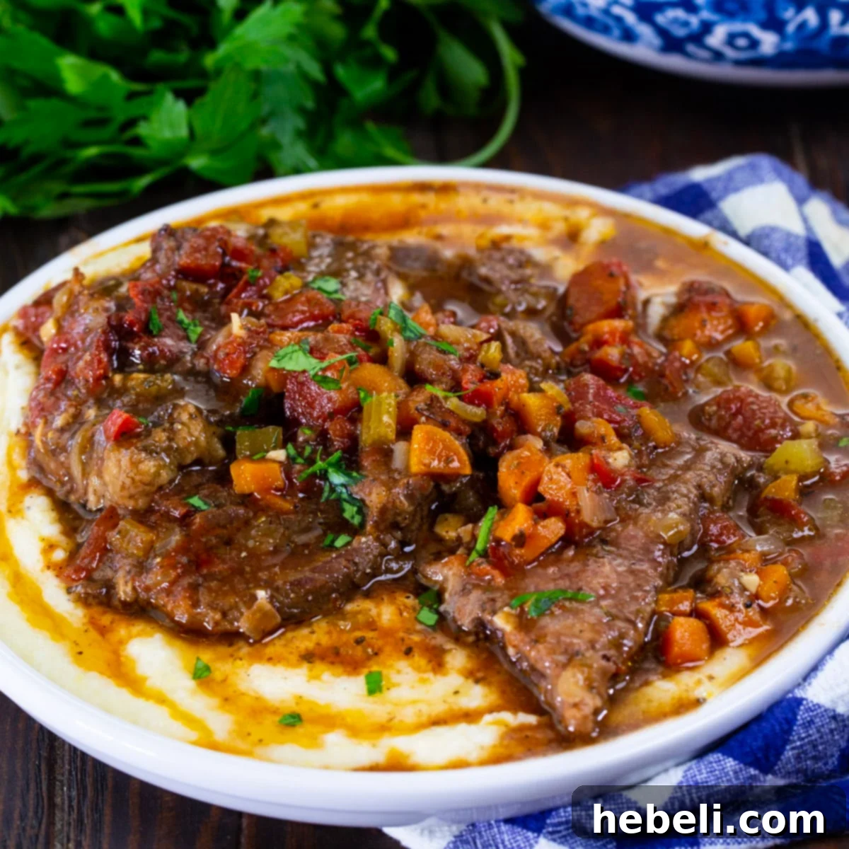 Fork Tender Slow Cooker Grillades 2 Slow Cooker Grillades over grits on a plate, garnished with fresh parsley.