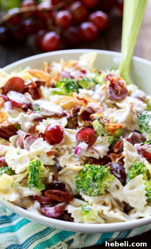 Sweet & Savory Broccoli Grape Pasta Medley 3 Broccoli Grape Pasta Salad in a white serving bowl, with a scattering of fresh red grapes in the background, highlighting its colorful ingredients.