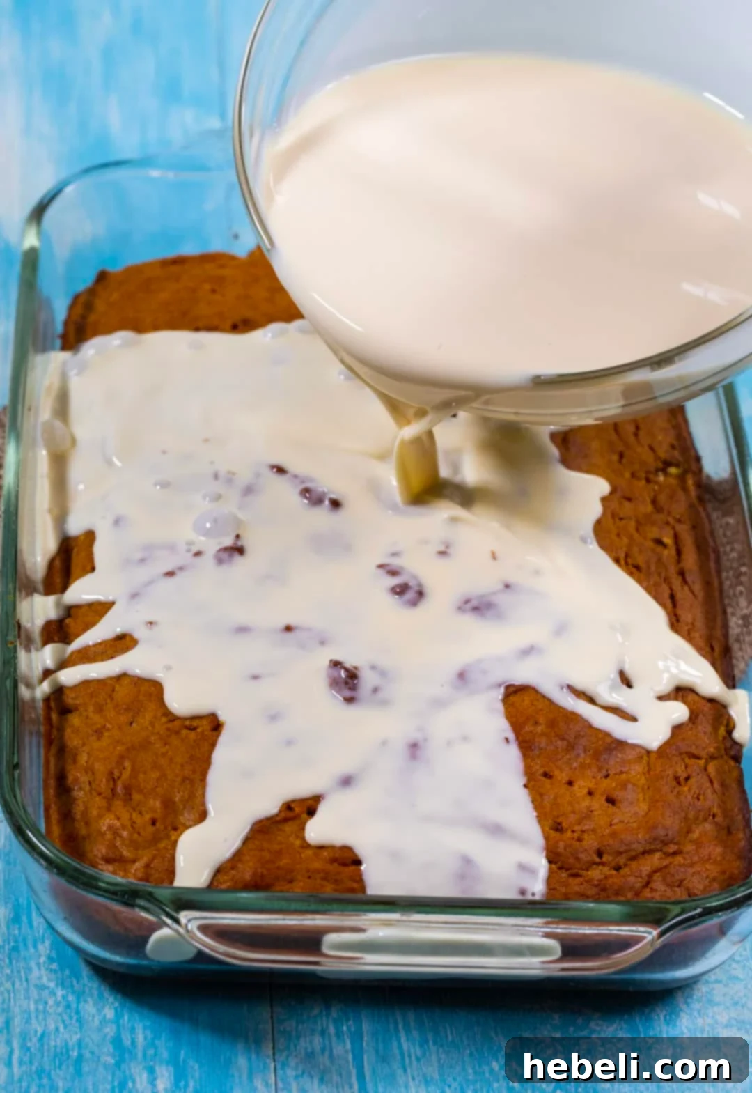 Spiced Pumpkin Tres Leches Cake 4 The three-milk mixture being slowly poured over the surface of a baked pumpkin cake in a baking dish.
