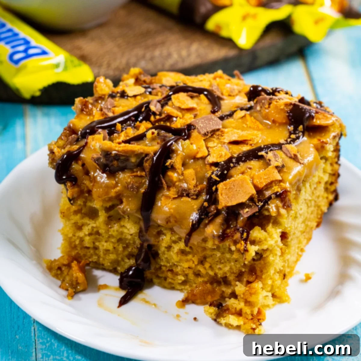 Crock Pot Butterfinger Cake 2 Square of Slow Cooker Butterfinger Cake on a plate, garnished with more Butterfinger pieces and chocolate drizzle.