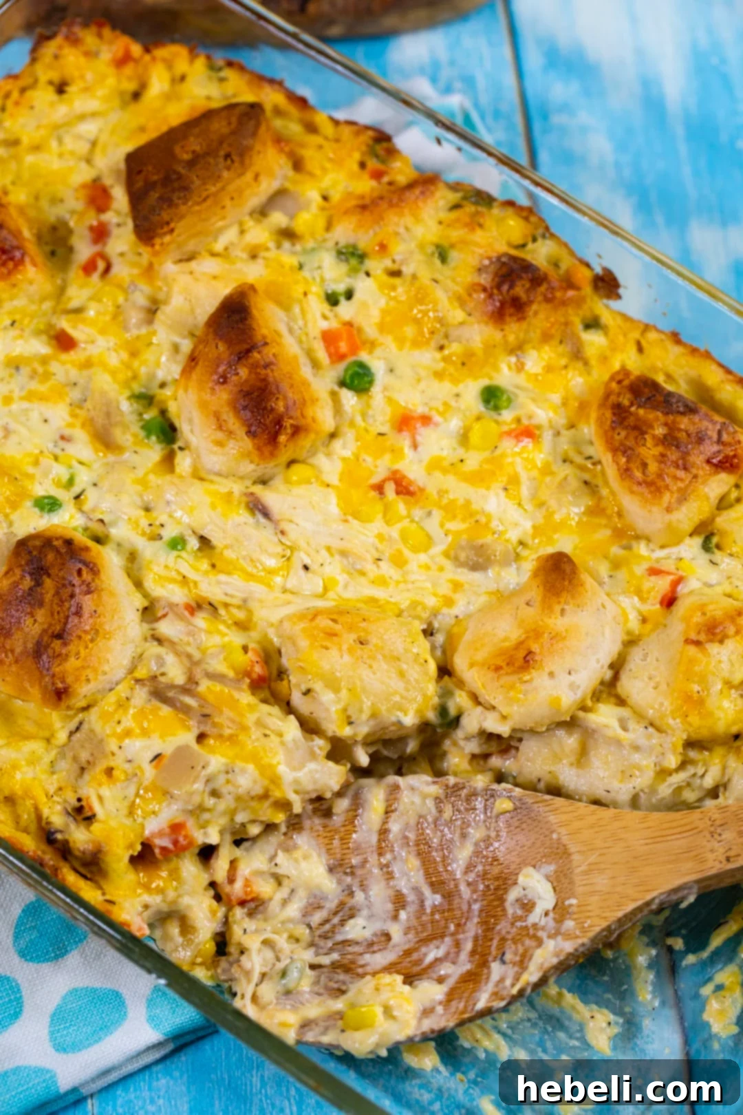 Fluffy-Topped Chicken Pot Pie Casserole 6 A wooden spoon scooping a generous portion of Chicken Pot Pie Bubble Up casserole from the baking dish, showing the creamy filling and biscuit chunks.