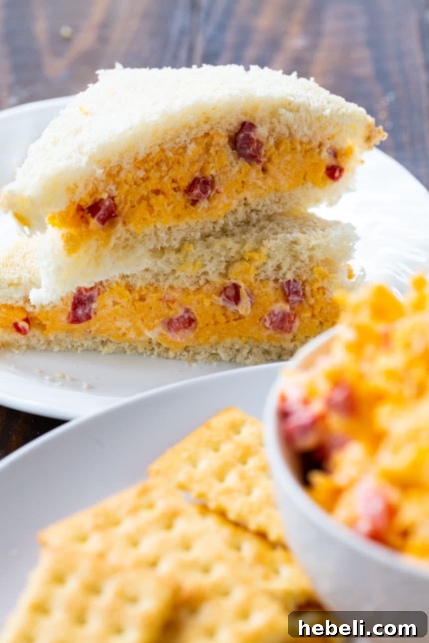 Southern Pimento Cheese Perfection 4 A close-up of a perfectly prepared Pimento Cheese sandwich on a white plate, showcasing the creamy, vibrant filling between soft white bread slices.