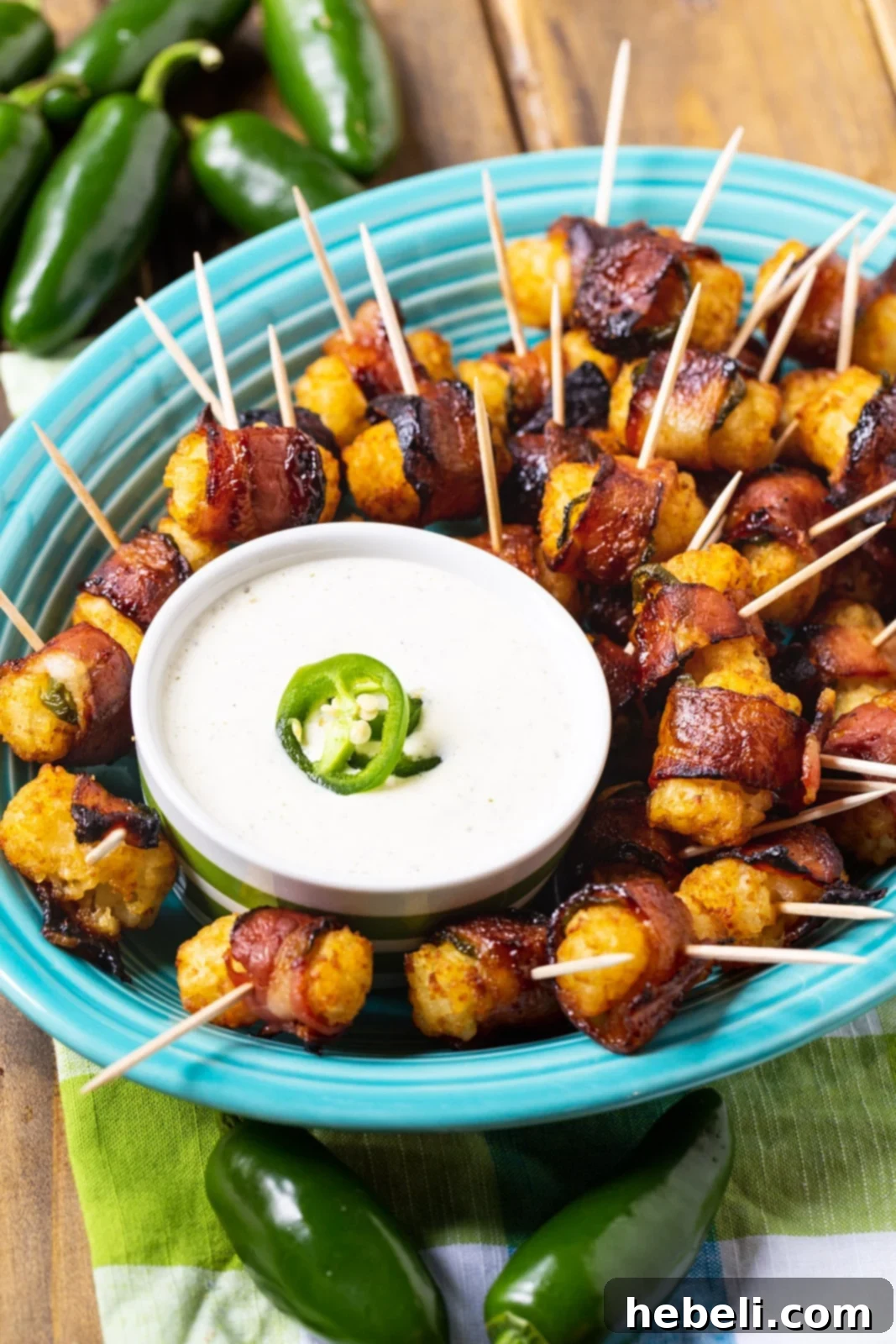 Perfectly cooked Bacon-Wrapped Tater Tots adorned with jalapeño slices, arranged on a vibrant blue serving plate alongside a small bowl of creamy ranch dipping sauce, ready to be enjoyed.