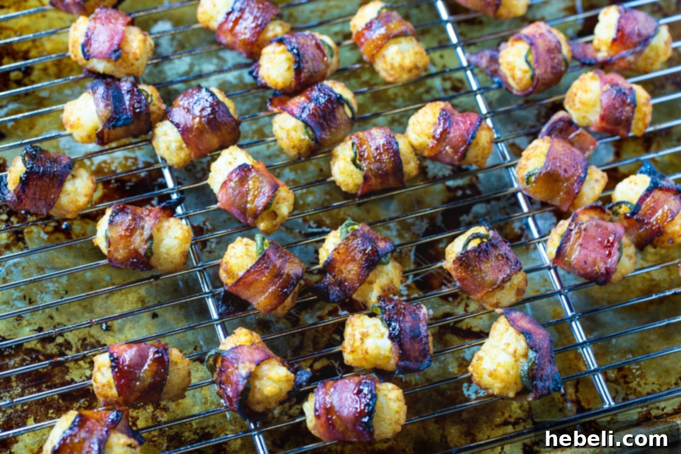 A tray of uncooked Jalapeño Bacon Tater Tots neatly arranged on a wire rack over a baking sheet, showcasing the bacon wrap and jalapeño slices before baking.