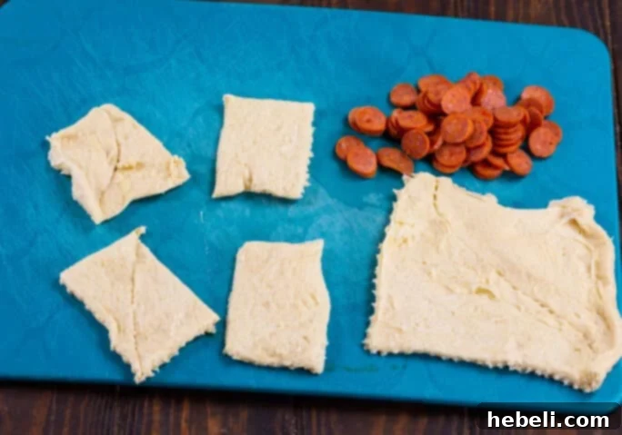 Cheesy Pepperoni Pizza Bites 4 Crescent roll dough rectangles being cut into smaller, more manageable squares, demonstrating a key preparation step.