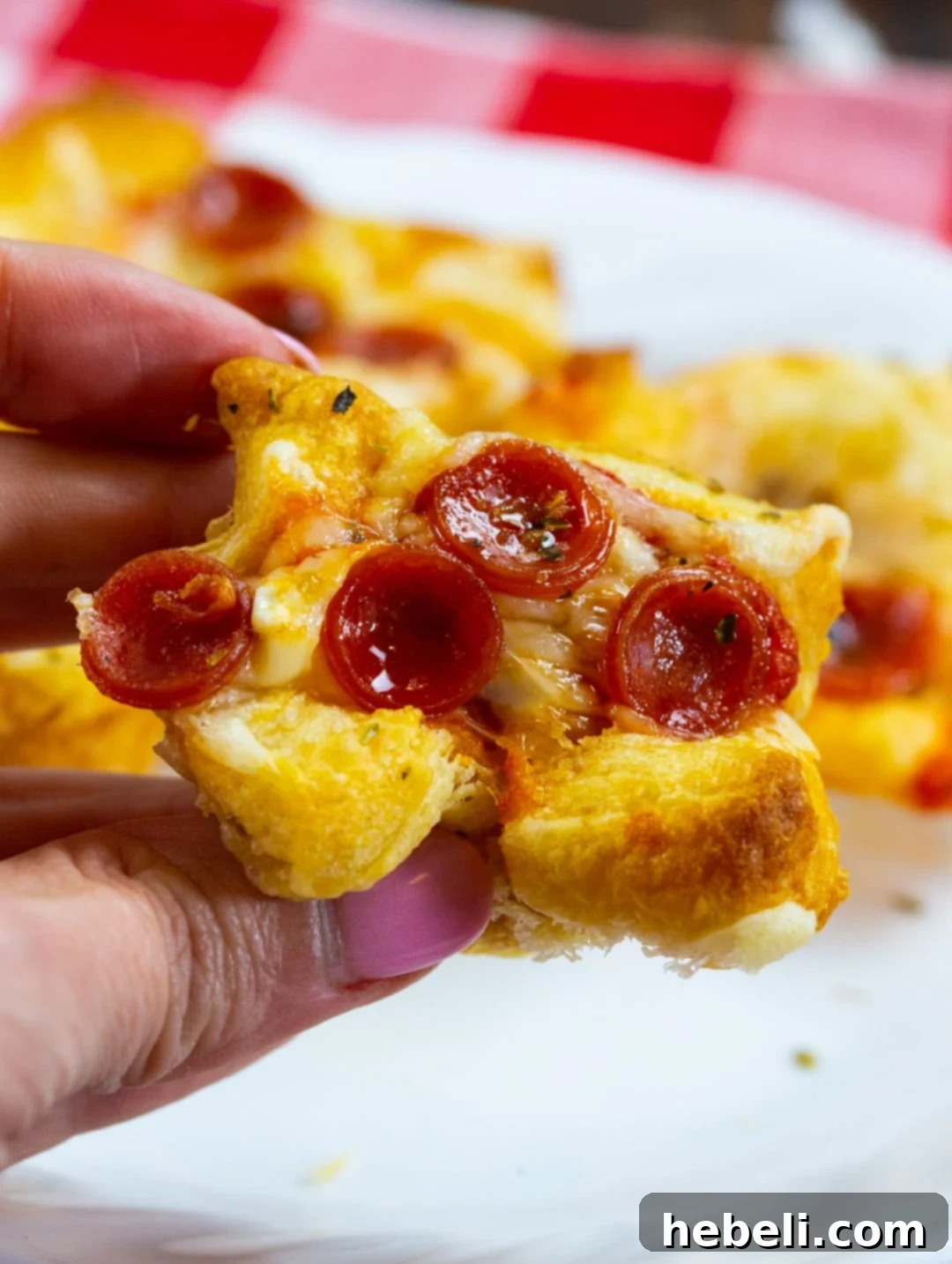 Cheesy Pepperoni Pizza Bites 6 A hand reaching into a mini muffin tin to grab a warm, freshly baked Pepperoni Pizza Popper, illustrating their irresistible appeal.