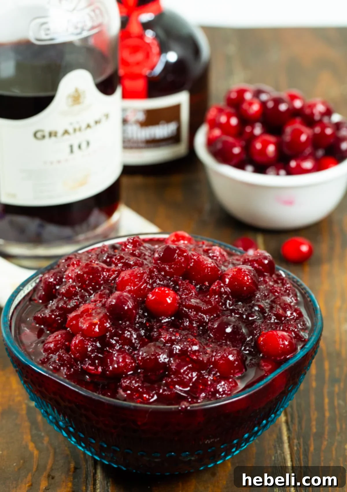 Cranberry Bourbon Relish 3 A bowl of freshly made Boozy Cranberry Sauce next to a bowl of vibrant, whole fresh cranberries, showcasing the primary ingredient.