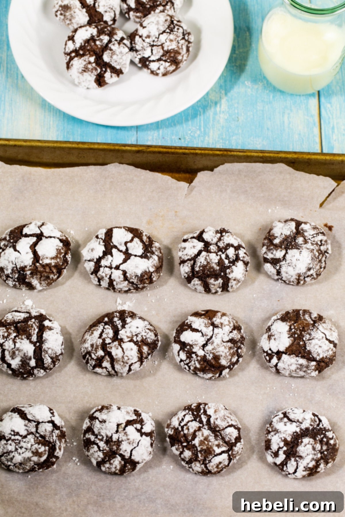 Close-up of baked Chocolate Peppermint Crinkle Cookies on a plate and a baking sheet, showing the perfect crinkles and powdered sugar.