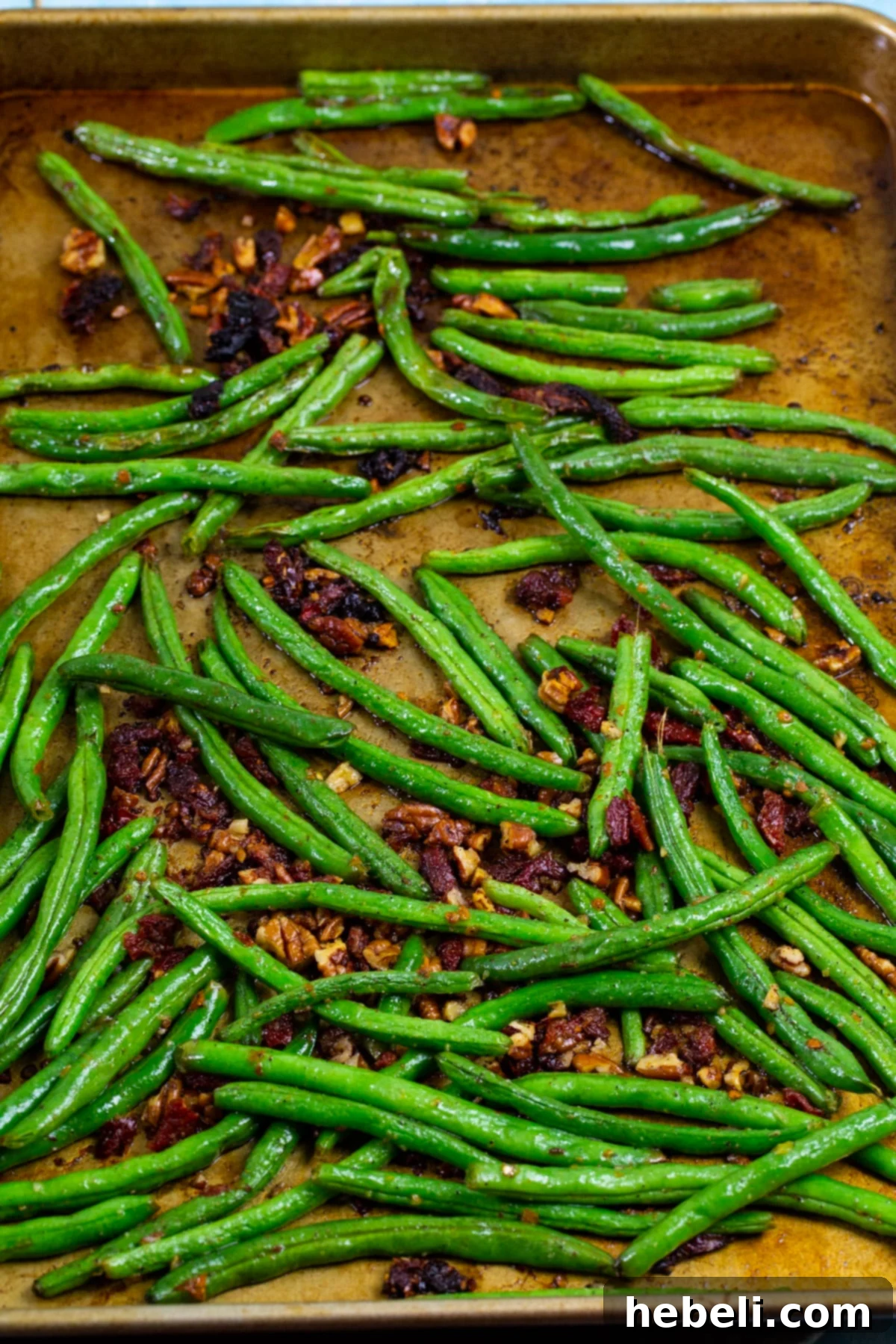 Mediterranean Roasted Green Beans with Sun-Dried Tomatoes 3 Fresh green beans spread out on a baking sheet, ready for roasting, with sun-dried tomatoes nearby.