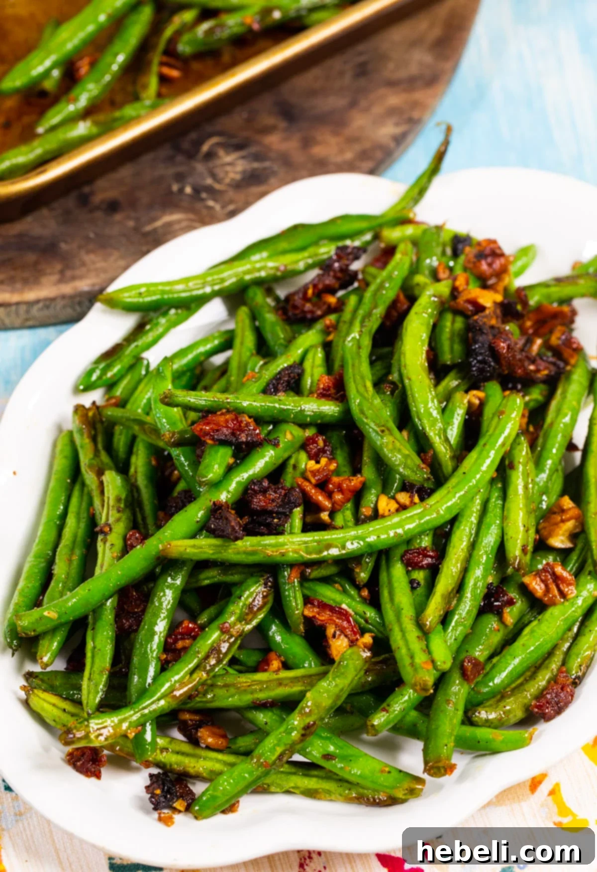 Mediterranean Roasted Green Beans with Sun-Dried Tomatoes 4 Close-up of roasted green beans with sun-dried tomatoes and toasted pecans on a serving plate, highlighting texture and color.