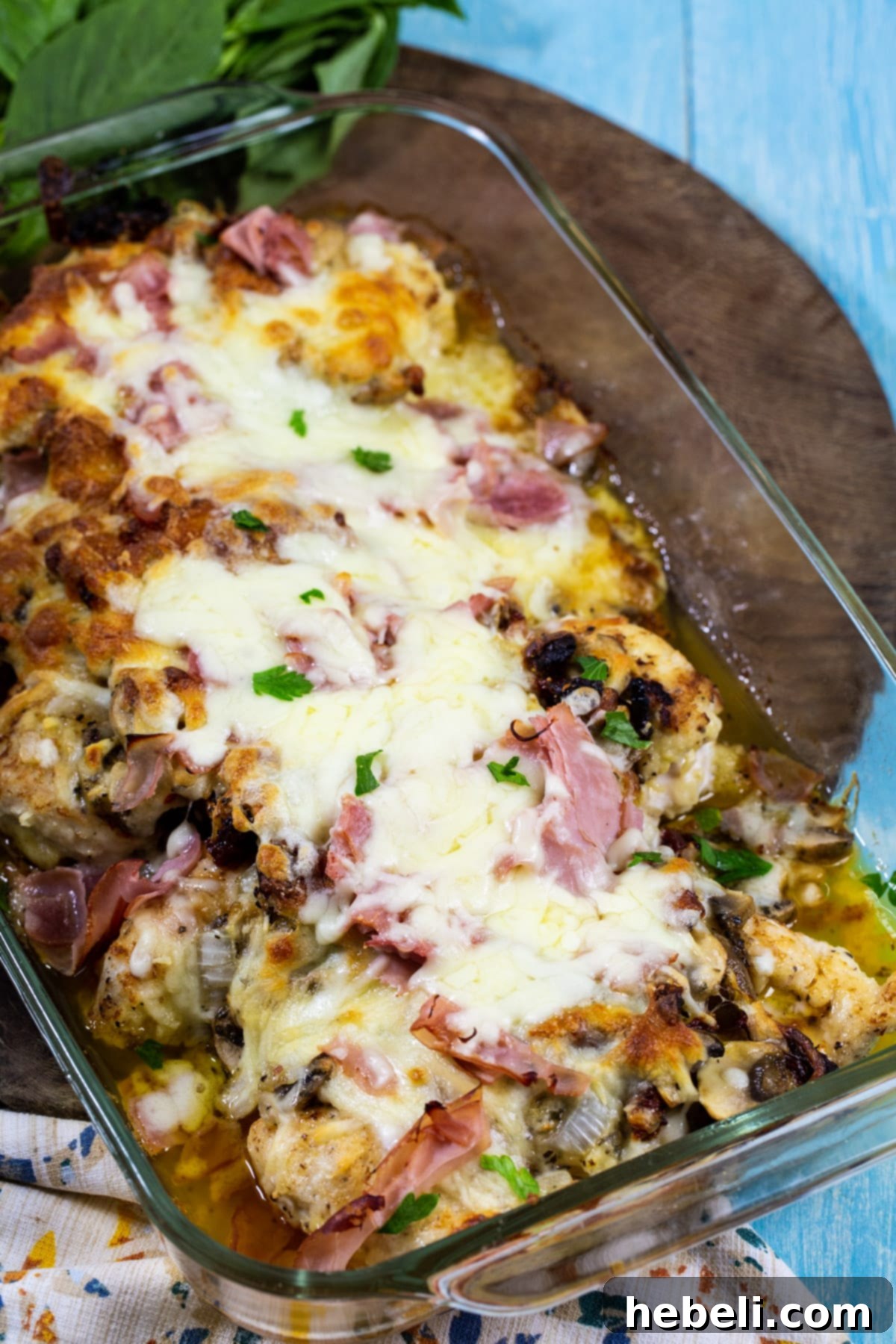 The Company Coop 4 Company Chicken topped with ham, mushrooms, and melted cheese, fresh from the oven, with a serving spoon.