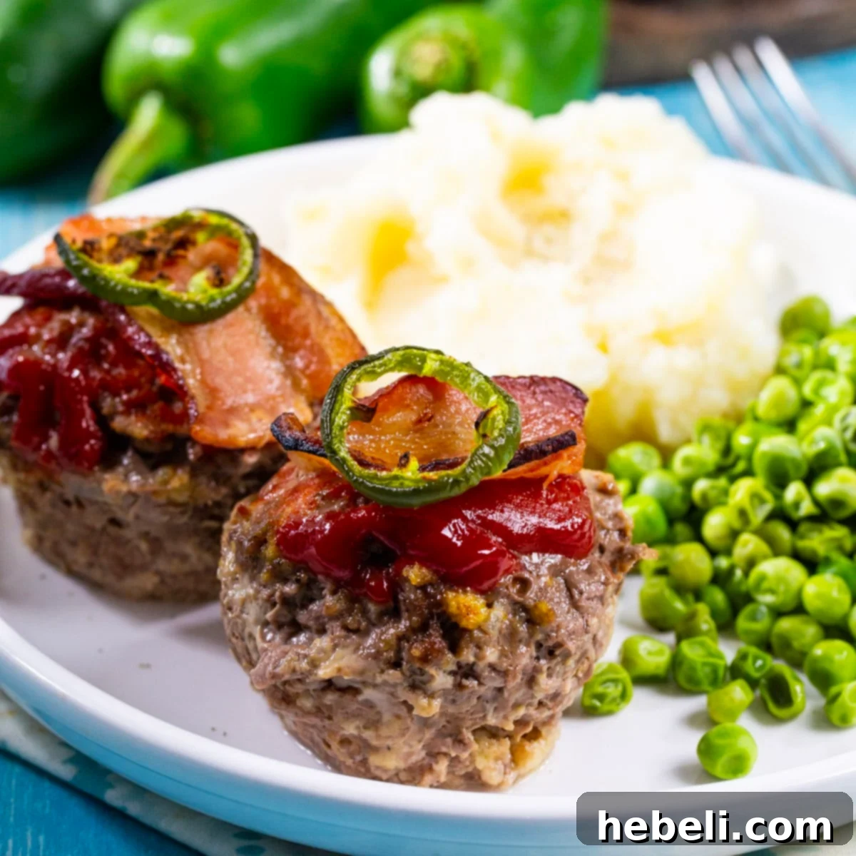 Two Jalapeno Popper Meatloaf Muffins on a plate, served with fluffy mashed potatoes and vibrant green peas.