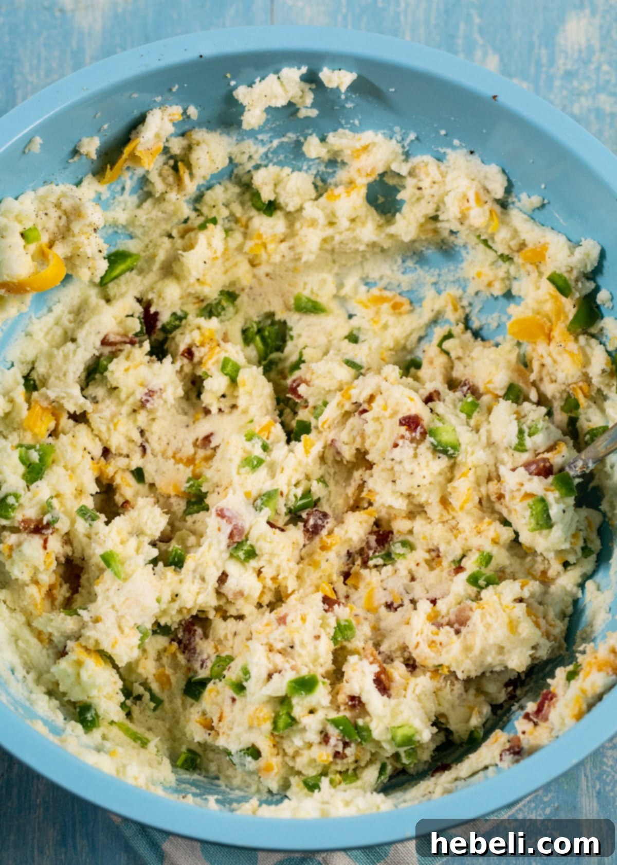 A large bowl filled with creamy potato filling, mixed with cheese, bacon, and jalapenos.