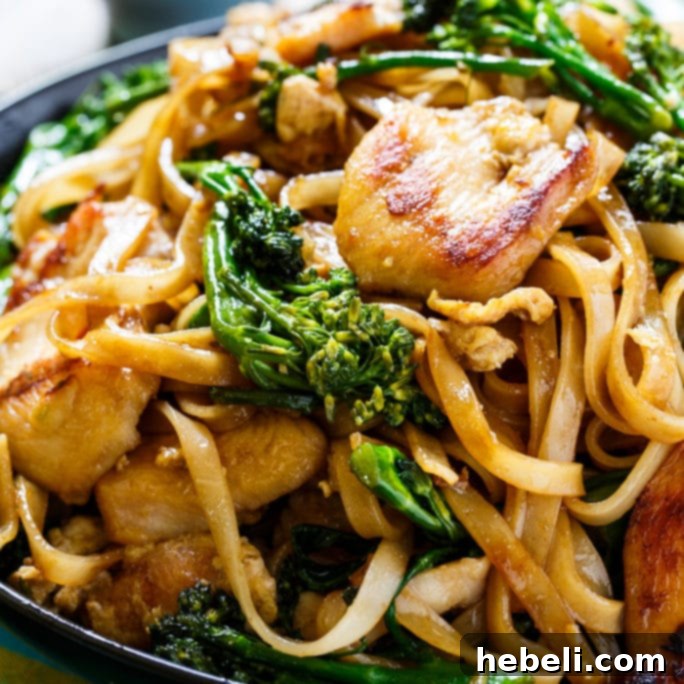 A perfectly portioned black bowl overflowing with delicious Thai-style stir-fried noodles, chicken, and crisp broccolini, ready to be enjoyed.