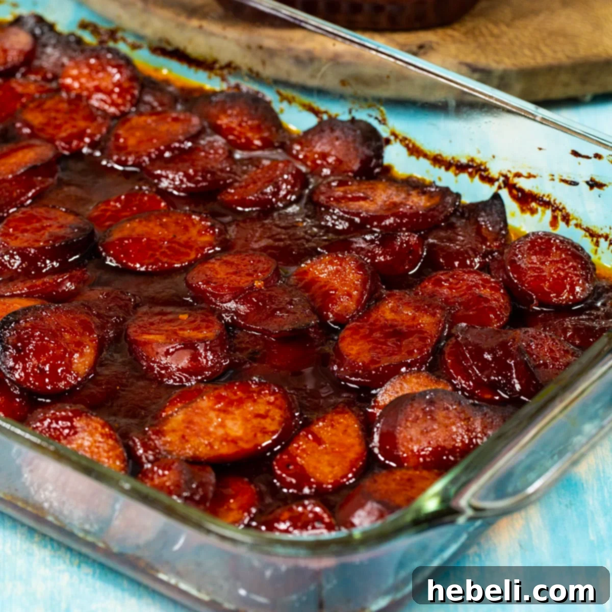 Baked BBQ Sausage in a glass baking dish, glistening with sauce and slightly charred edges, ready to serve.