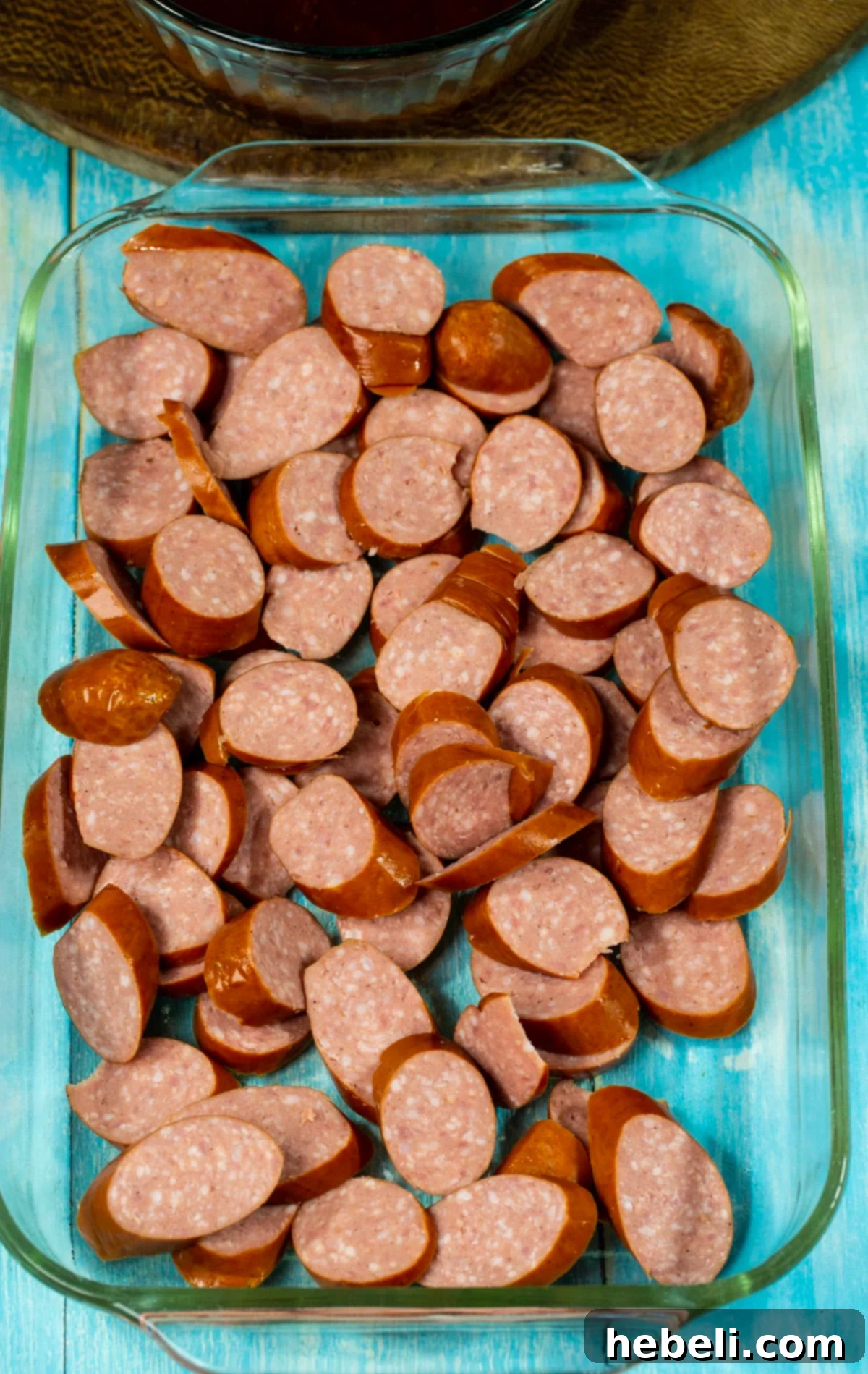 Uncooked kielbasa sausage slices arranged in a baking dish before sauce is added.