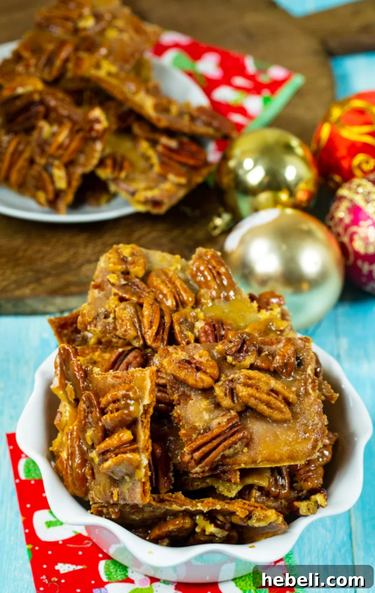 Pieces of Pecan Pie Bark arranged in a serving dish with holiday ornaments in the background.