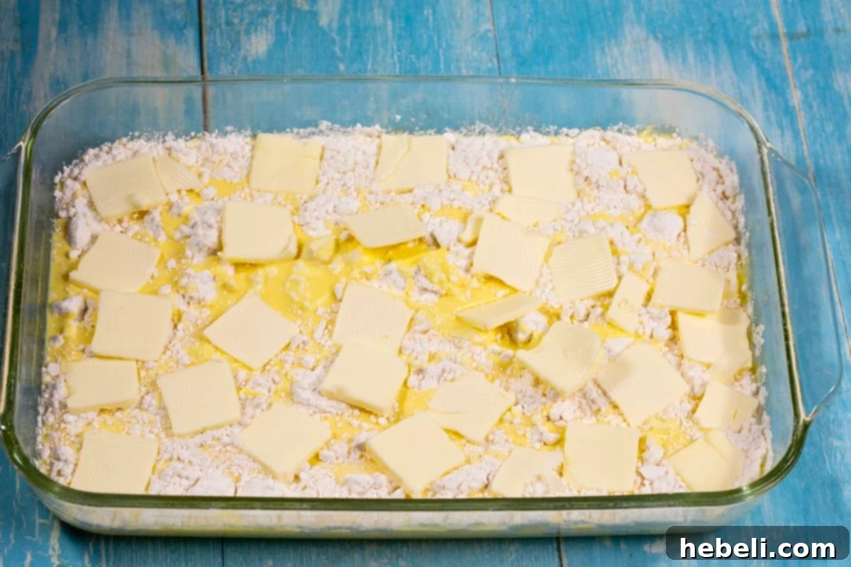An assembled 3-Ingredient Eggnog Dump Cake in a baking dish, with eggnog, cake mix, and butter slivers layered, ready for the oven.