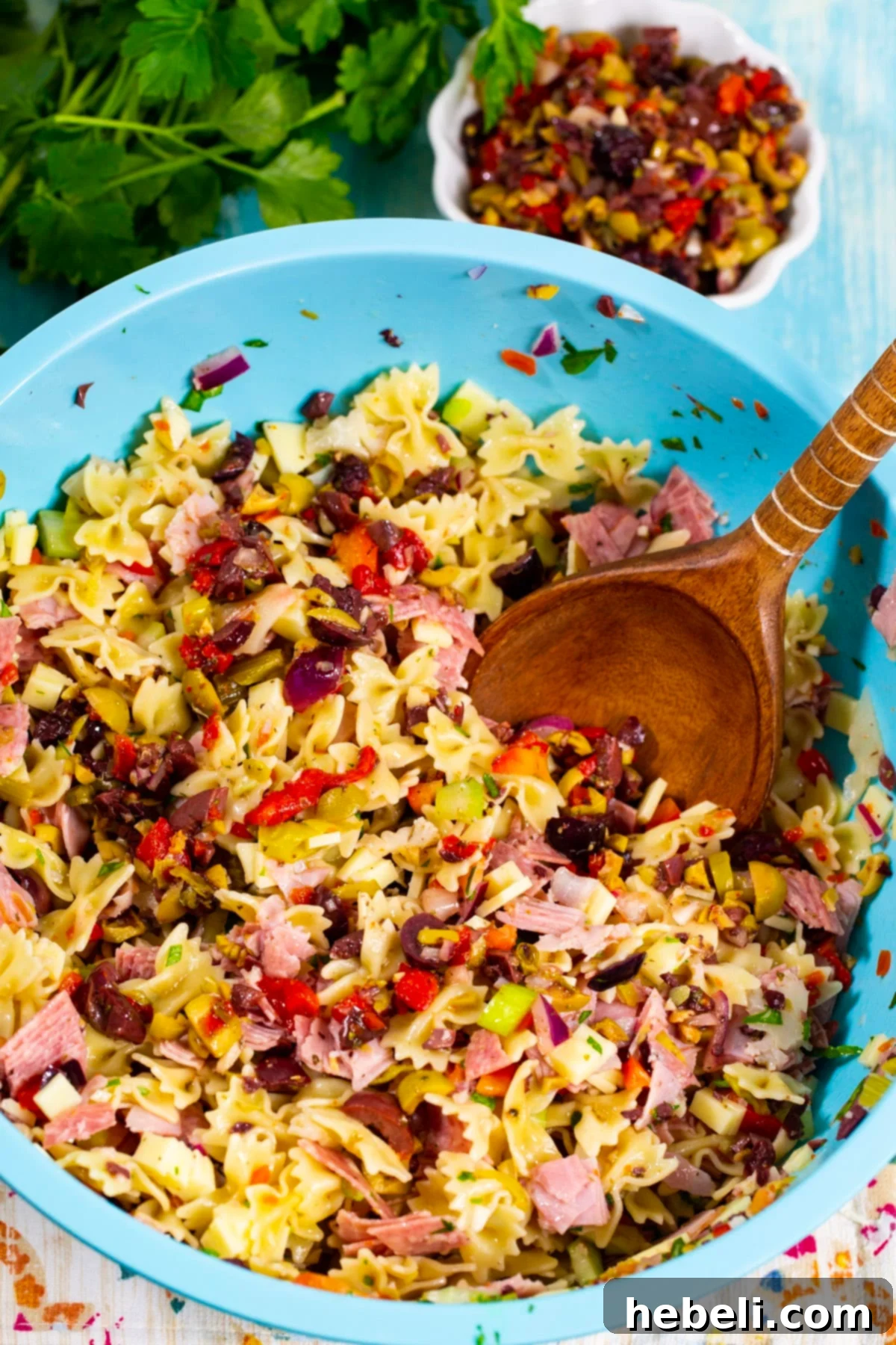 Zesty Muffaletta Pasta Salad 3 Preparing Muffaletta Pasta Salad: Pasta and fresh ingredients in a mixing bowl, alongside a small bowl of olive salad.