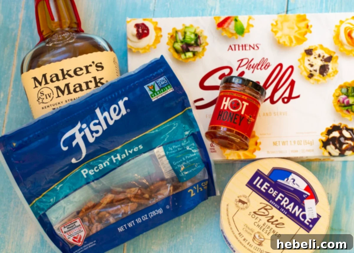 A visual guide to the five essential ingredients for Bourbon Pecan Brie Bites: phyllo cups, a wheel of brie, chopped pecans, a bottle of hot honey, and a glass of bourbon.