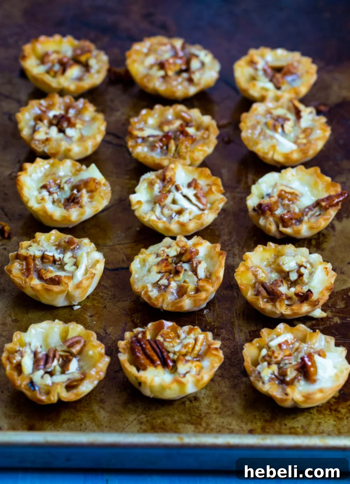 A baking sheet filled with freshly baked Bourbon Pecan Brie Bites, their phyllo cups golden and crisp, the cheese melted and bubbling.