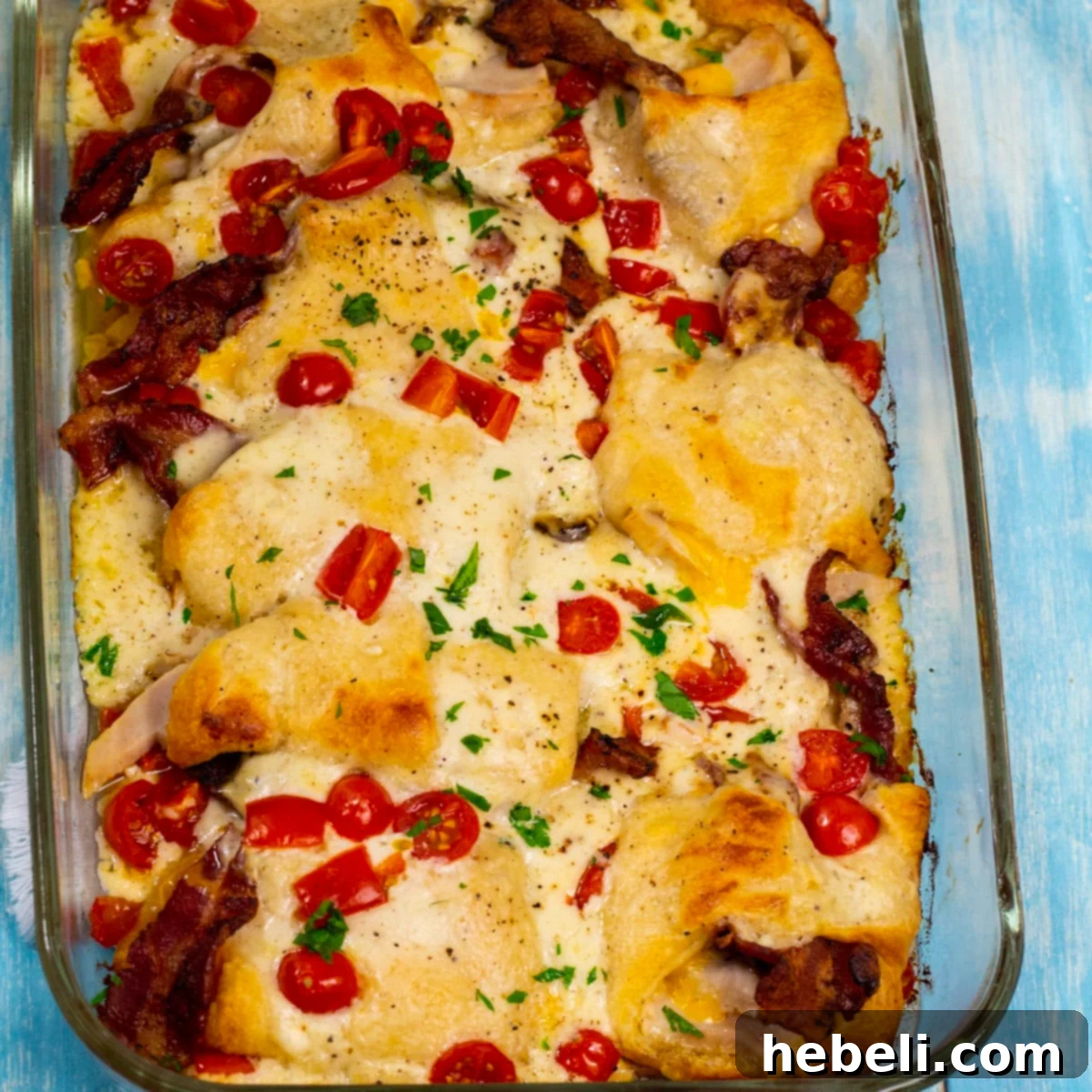 Kentucky Hot Brown Crescent Bake 2 A golden-brown Kentucky Hot Brown Crescent Casserole, freshly baked in a rectangular baking dish, topped with melted cheese, crispy bacon, and bright cherry tomato halves.