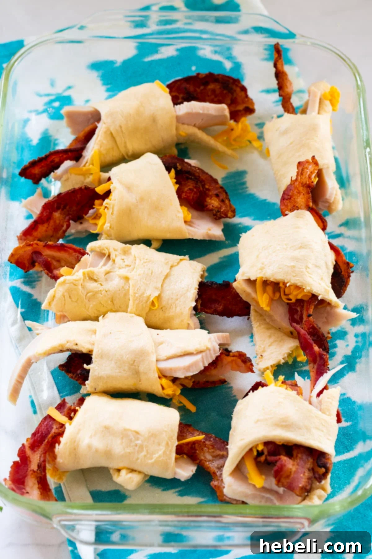 Kentucky Hot Brown Crescent Bake 6 An overhead shot of the Kentucky Hot Brown Crescent Casserole in its baking dish, showcasing the golden crescent rolls coated in Mornay sauce, with bacon and tomatoes visible.