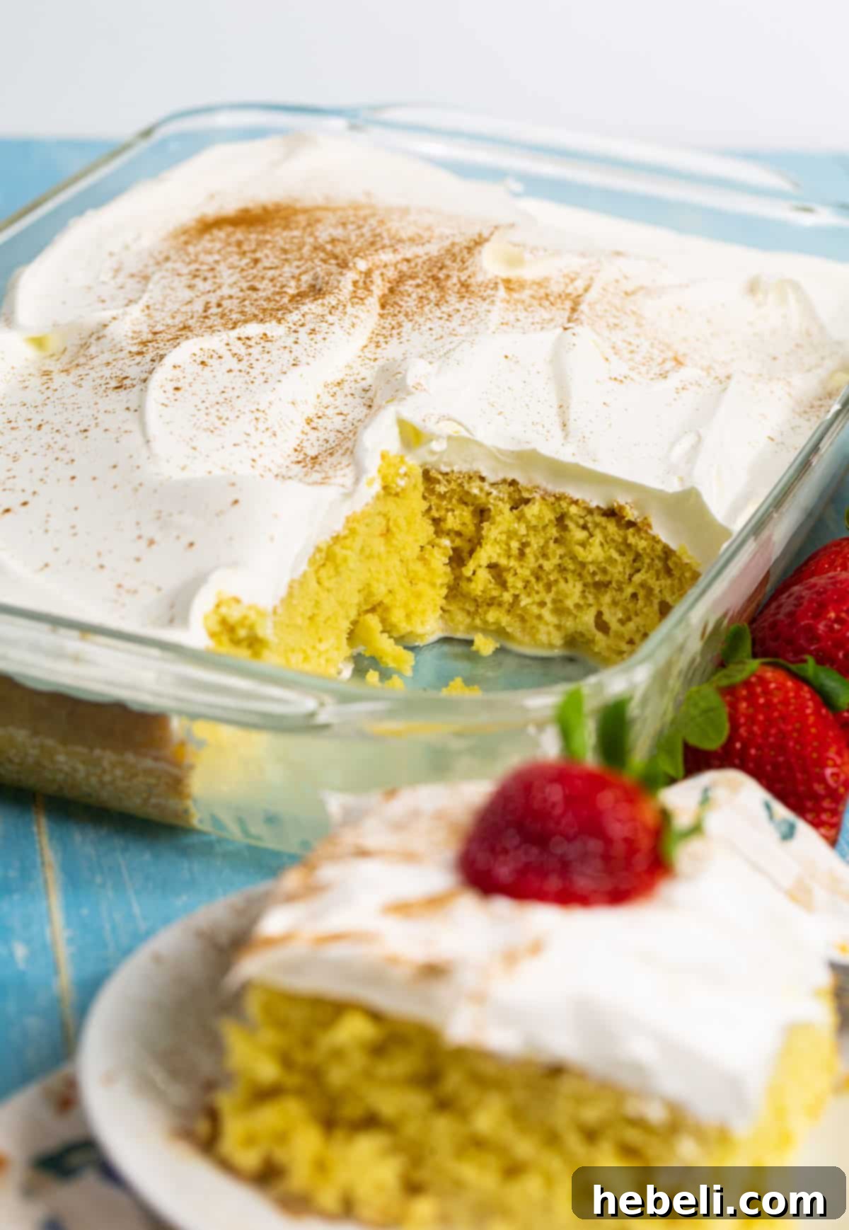 Effortless Tres Leches Cake 5 A full Tres Leches Cake in a baking dish, with one slice neatly cut out, showcasing its moist interior and creamy topping.