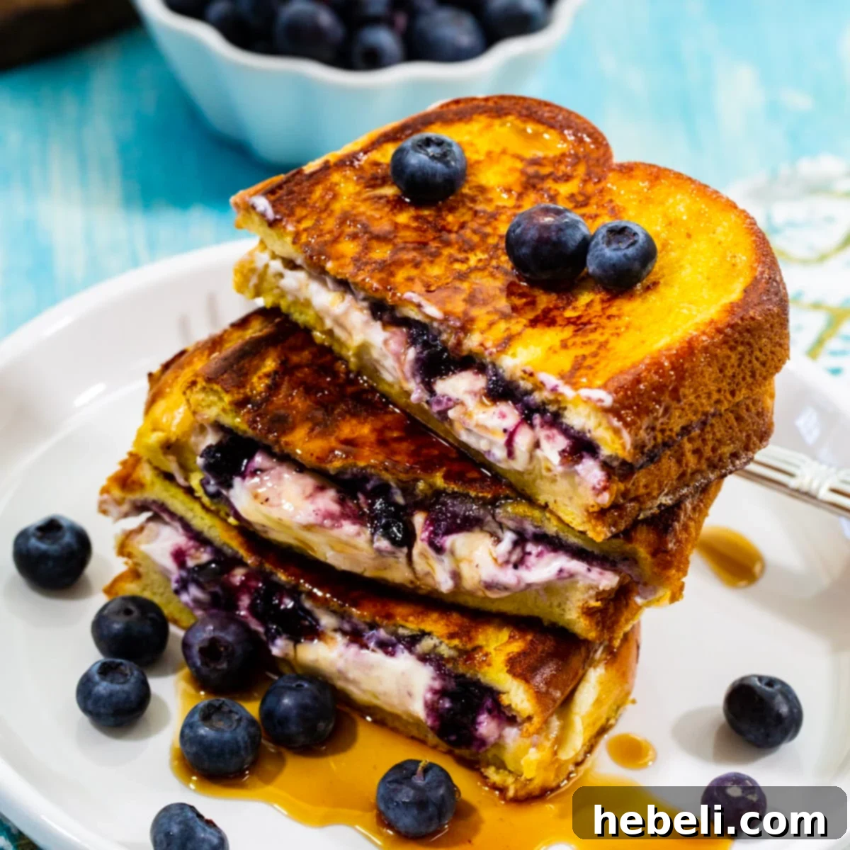 Stacked slices of golden-brown Blueberry Stuffed French Toast on a white plate, ready to be served.