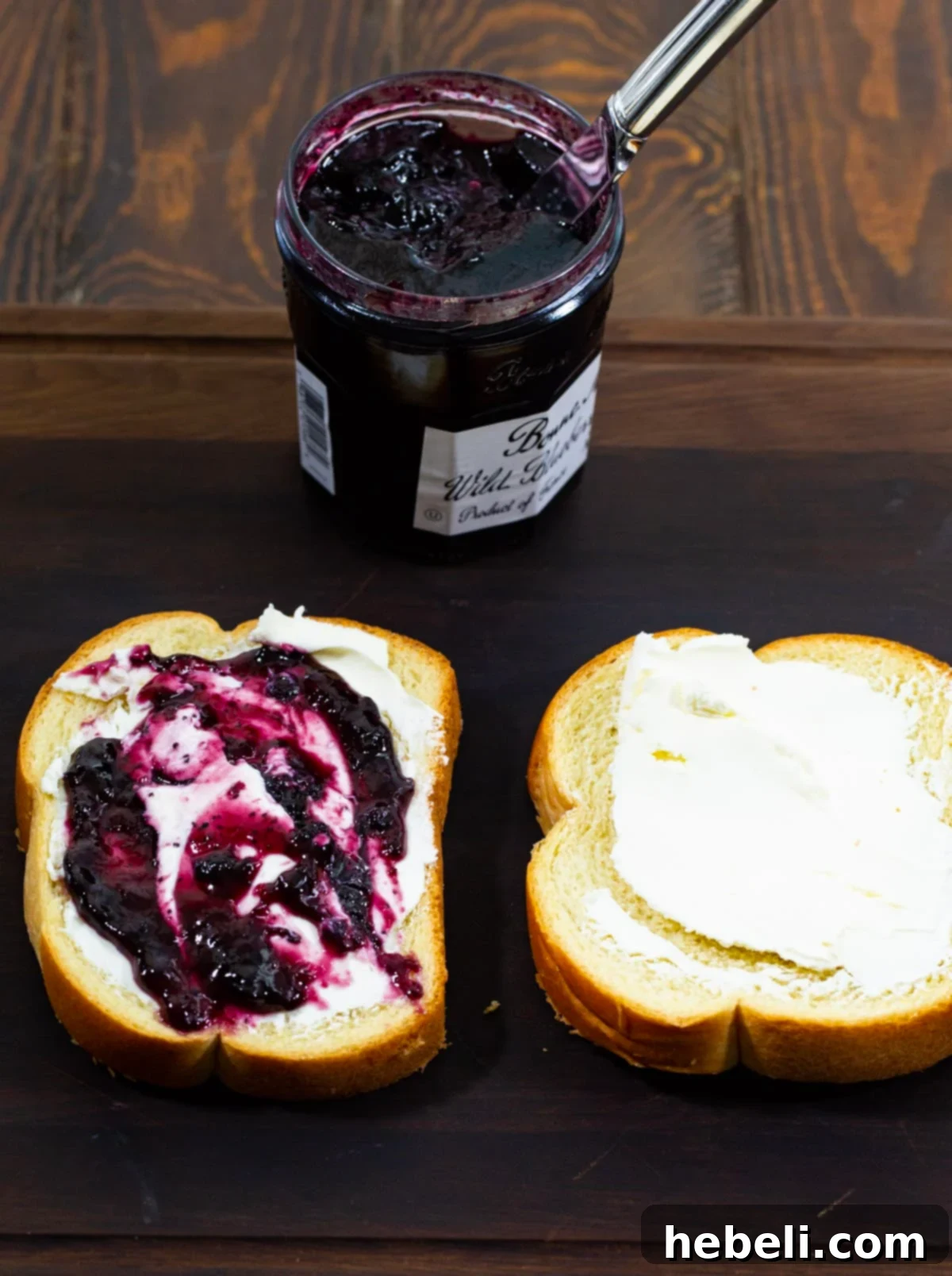 Close-up of cream cheese and blueberry preserves being generously spread onto slices of brioche bread, preparing them for the delicious French toast filling.