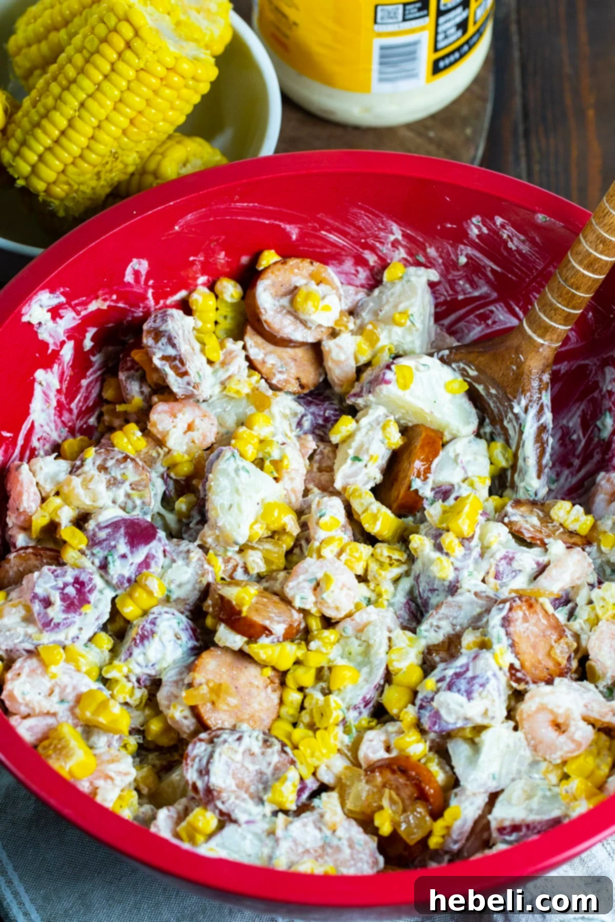 Freshly prepared Frogmore Potato Salad being mixed in a large bowl, showing its creamy texture and vibrant ingredients.